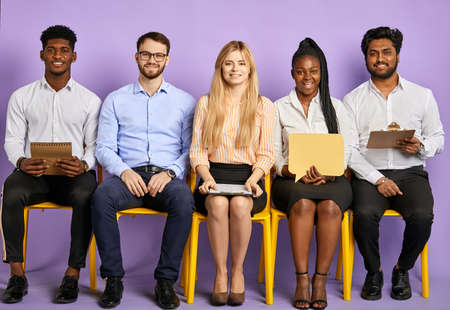 Diverse group of multinational young people smiling and looking in camera waiting for job interviewの写真素材