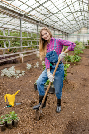 awesome girl dressed in shirt and overall holding a shovel and posing to the camera. full length...
