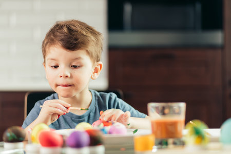 4-year old caucasian boy helps his mother with preparations to Easter. Concentrated kid is engaged...