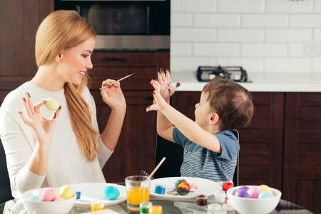 Its a gift, being good with kids. Attractive blonde woman painting colorful easter eggs with her amazing son. Family celebrating Easter. Parent and kid play indoors.の写真素材