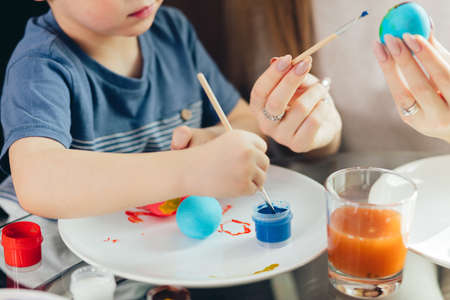 Young beautiful mother, being great with her adorable son, spend time together. Easter celebration and parenthood concept. Mother and son making Easter decorations at home.の写真素材