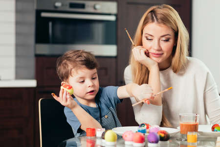 Young beautiful mother, being great with her adorable son, spend time together. Easter celebration and parenthood concept. Mother and son making Easter decorations at home.の写真素材