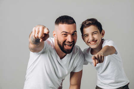 laughing daddy and son pointing at the camera. close up shot. happiness, positive emotion. isolated grey background. funの写真素材
