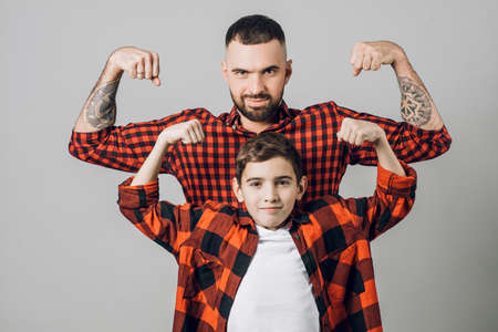 Handsome bearded strong father and his son looking at camera while showing biceps. close up shot. strength, power, fitness, bodybuilding, sportの写真素材
