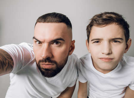 puzzled two brothers are taking photos. close up portrait. first selfie. handsome man and his son using camera for the first timeの写真素材
