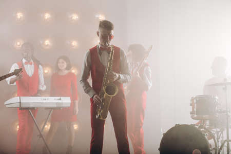 handsome talented saxophonist playing jazz music indoors. close up photo.retro partyの写真素材