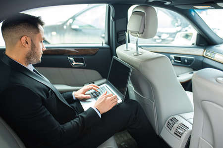 Confident man in tuxedo sit using laptop, working in car, man with beardの写真素材