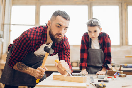 Bearded jointer man in safety glasses and an apron works with chisel in a carpentry shop. Carpenter...