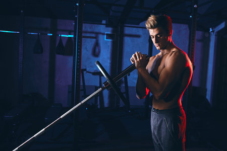 Caucasian muscular shirtless bodybuilder, flexing weight plates on iron bar over smoky dual color...