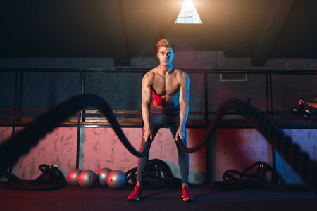 Caucasian shirtless athlete practicing Battle Rope Exercise, great for improvement of Athletic...
