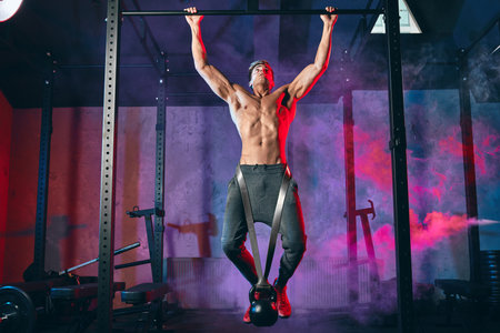 Young bodybuilder training in the gym exercising Wide-Grip Pull-Up with weight. Fitness man pumping...