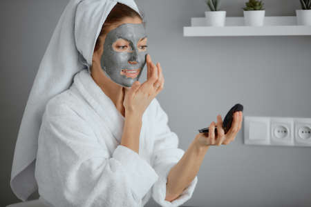 beautiful caucasian woman in white bathrobe and towel use beauty procedures sitting at home after showerの写真素材