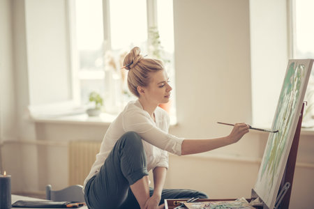 fair-haired female freelancer working at home. close up side view photo.windows with flowers in the...