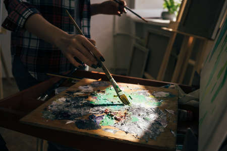 womans hand with brush mixing paints in the dark room. close up cropped photo.の写真素材