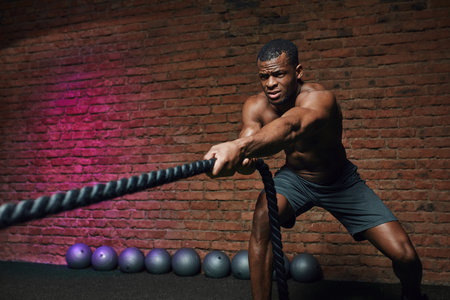 African cross fit coach stands with battle ropes proves that dynamic workout with ropes...