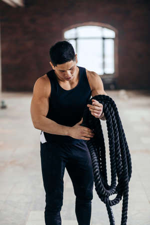 young sportsman choosing a rope for training. athlete preparing for battle rope workout. close up shotの写真素材