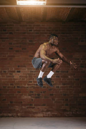 African athletic man with naked torso jumping high in air during crossfit workout. Lifestyle Sport Power and Emotional Success Concept.の写真素材
