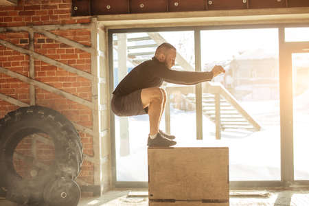 Caucasian determined sportsman performing plyometric box jumps indoor, in crossfit functional workoutの写真素材