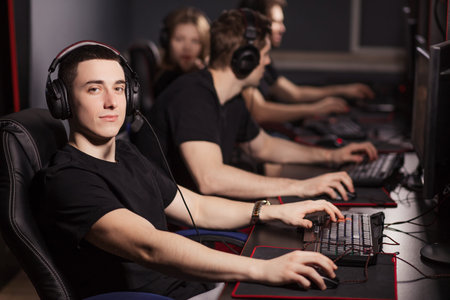 Satisfied smart gamer in black t-shirt sitting behind the computer monitor and looking at camera in...