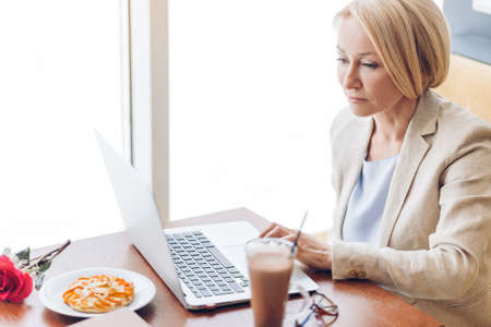 gorgeous mature woman looking at the photos on the laptop. close up side view photo. online date. holiday, day offの写真素材