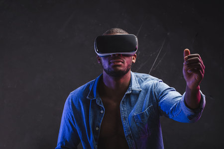 African man in denim unfasten shirt using headset, experiencing virtual reality while playing video...