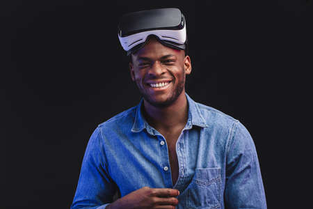 Surprised beard man taking off his virtual reality glasses from his head, on black backgroundの写真素材