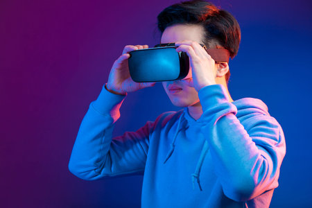 Young Asian man playing VR game in dark blue background. Chinese young hipster wearing VR headset,...