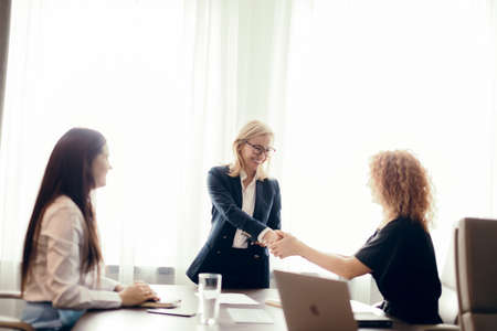 Group of business women meeting at the office. Blonde woman dressed in formal suit sharing her ideas with two colleagues, sitting at the desk.の写真素材
