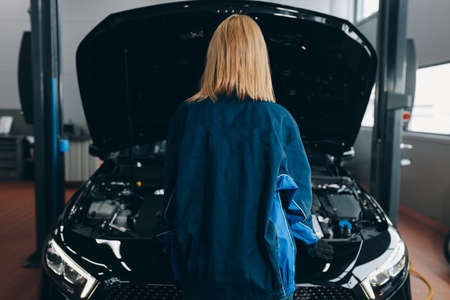 blond woman standing in front of the car with opened hood. close up back view photoの写真素材