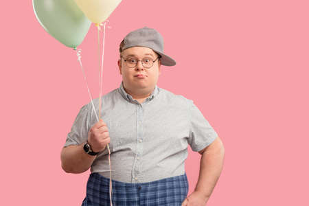 Ready to celebrate birthday. Adult grown up tubby man looks and dressed as a child posing with air ballons, looking at camera with childish naivety. Gift, birthday party concept.の写真素材