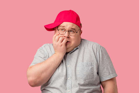 Overexcited plump man closes mouth with hands making bugged eyes, expresses fear or astonishment over pink studio background. Expressive facial expressions.の写真素材