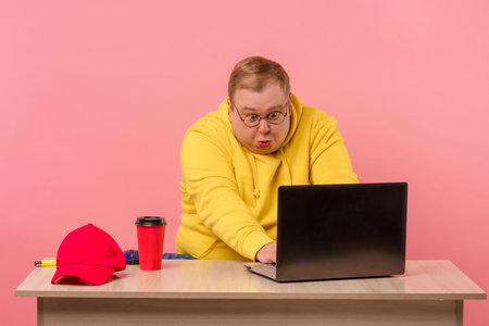 Cute comic man in bright colors casual wear geek working on computer with funny stupid facial...