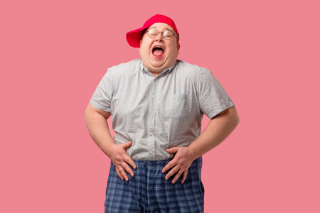Tubby softie man in red baseball cap laughs happily, holding his hands on belly, being in good mood,...