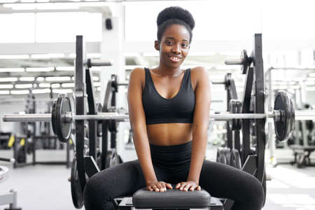 portrait of adorable african lady sitting in gym, young lady in sportswear after crossfit exercises, posing, smile. healthy lifestyle conceptの写真素材