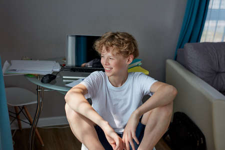 young caucasian teenager boy have rest after doing homework, sits on chair in bedroom and smile, leisure timeの写真素材