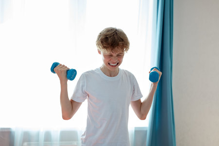 sportive child boy exercising with dumbbells at home, young caucasian teenager boy pump arm muscles