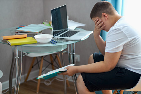 school boy tired to study, to do homework at home, sit depressed and exhausted. at home in bedroomの写真素材