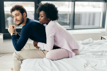 Portrait of young mixed race loving couple having romantic times in bedroom. African woman embracing affectionately from the back her european american friend.の写真素材