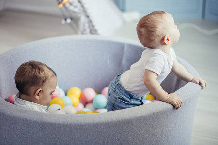 Two happy cute one year old infant boys are playing with colourful balls in a dry pool. Happy...