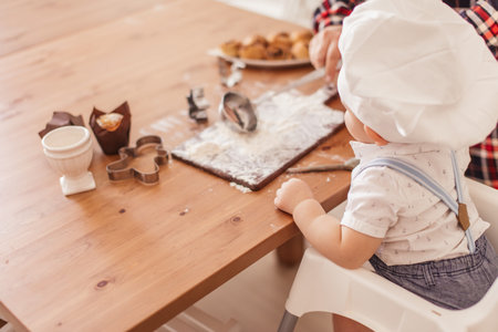 Charming toddler male baby playing as a cooker, dressed in white t-shirt and Chef hat sitting on...