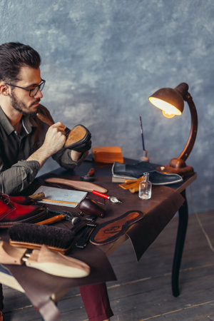 bearded male cleaning the heel of the shoes while sitting at the desk with lamp. close up photo