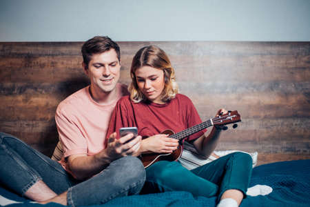 caucasian couple study to play ukulele together at home, look at screen of smartphoneの写真素材