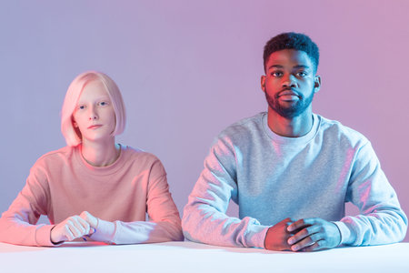 serious young multiethnic couple sitting at table and looking at camera, students listening to the...
