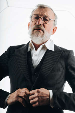 Bearded grey haired stylish elderly business man adjusting formal black suit, prepares to his final meeting before retirement, isolated over white backgroundの写真素材