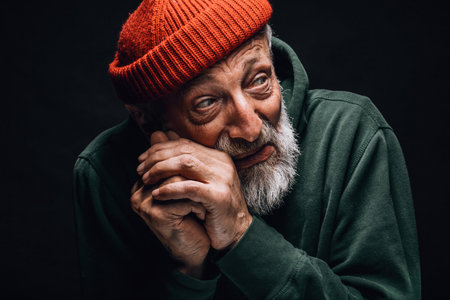 Frightened bearded homeless tramp man coweres, defending himself from a blow, isolated over black...