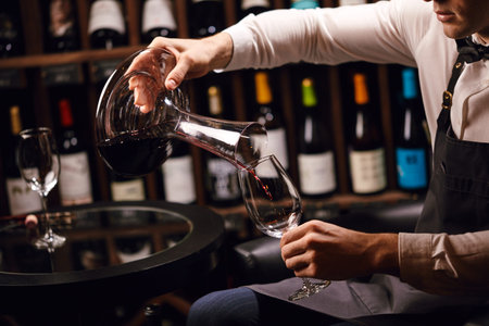 Wine taster or degustator mixing red wine into carafe to make perfect color on background with wine...