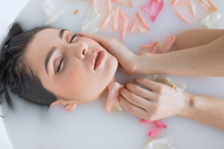 Luxury spa: passionate girl with silky skin relaxing laying in water bath with closed eyes, filled...