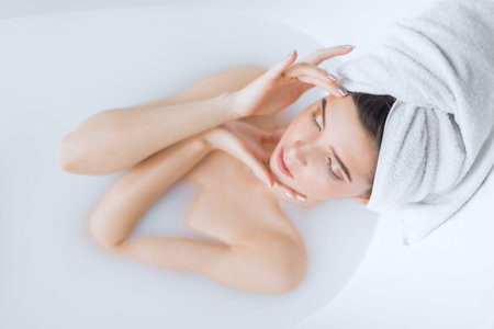 High angle viewof cute caucasian female model with perfect slim figure lying in milky water in...