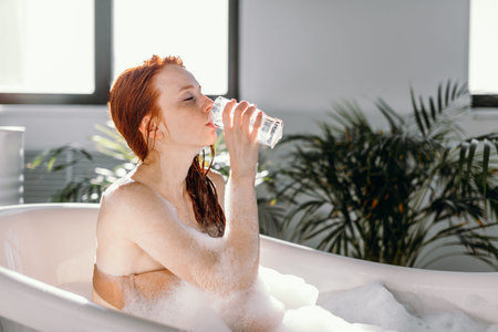Attractive red-haired young female tourist relaxing in bathtub of Hotel Spa, enjoying tranquillity that combines harmonious design elements with premium therapeutic treatmentsの写真素材