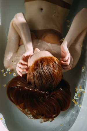 Sensual beautiful redhead woman with perfect smooth skin and frigile slim body relaxing in bathtub...